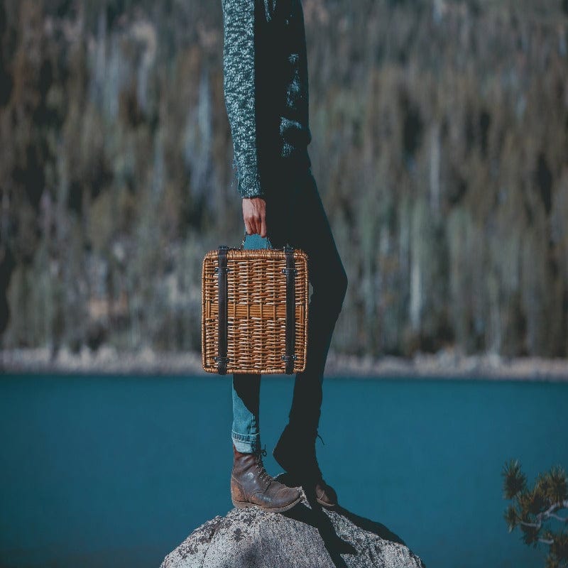 Picnic Time Champion Picnic Basket - Black with Brown Accents - Man carrying the Picnic Basket on top of a rock at a lake