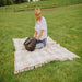 Picnic Time Montecito Picnic Blanket with Harness - Beige Gingham - woman sitting on blanket on grass