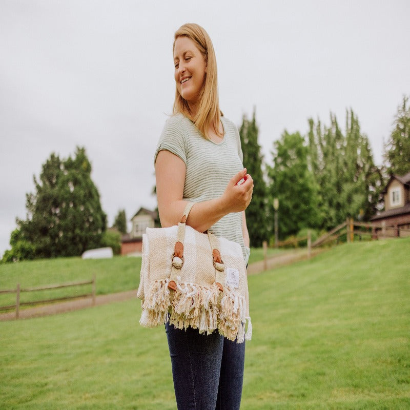 Picnic Time Montecito Picnic Blanket with Harness - Beige Gingham - woman carrying blanket by its harness