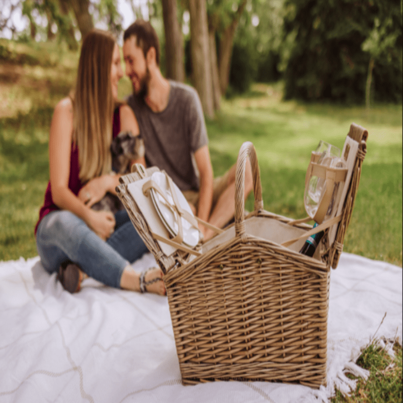 Picnic Time Piccadilly Picnic Basket - Natural Canvas- man and woman on picnic blanket with picnic basket open