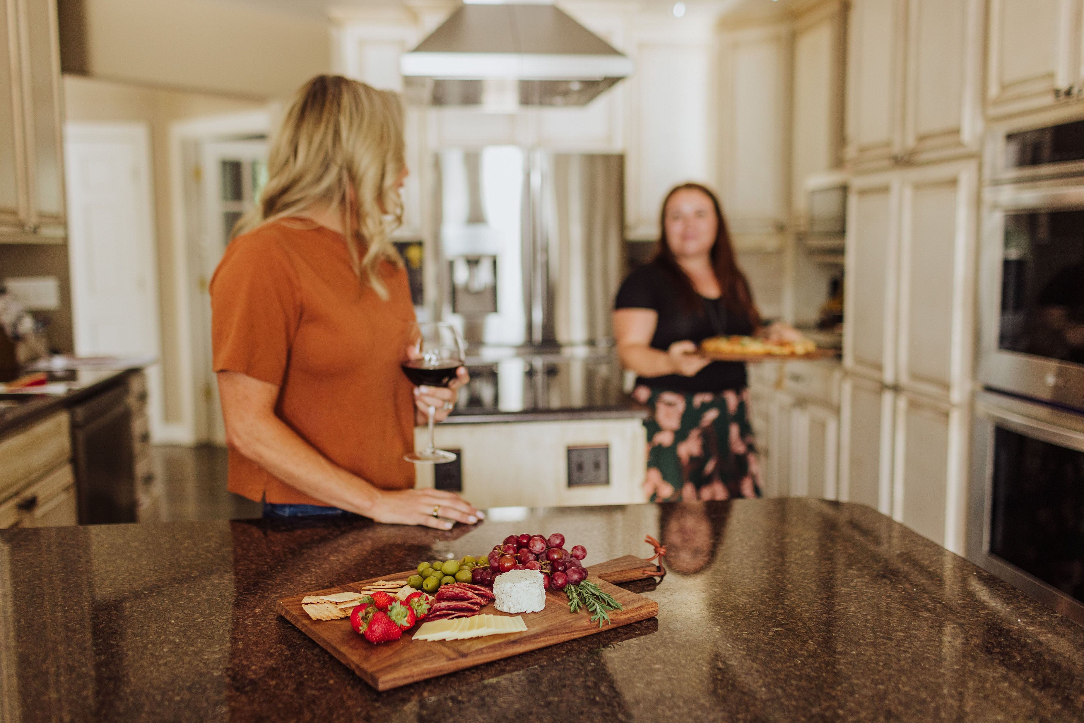 Toscana Madera Rectangular Charcuterie Board - board on kitchen counter with woman and wine glass