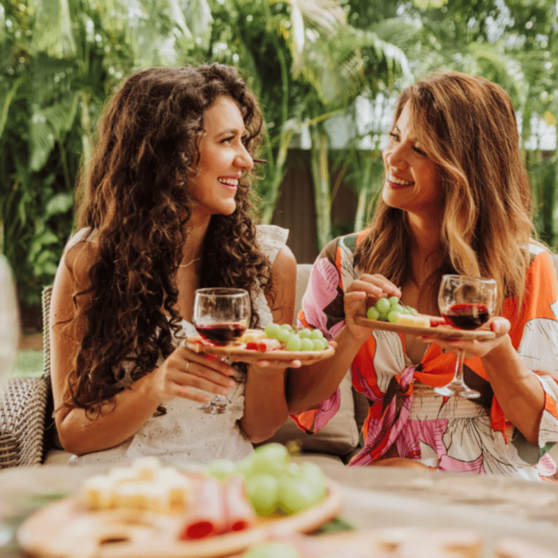 TOSCANA ENTERTAINING WINE AND APPETIZER PLATE, SET OF 4, IN ACACIA WOOD-showing 2 female humans each holding a full appetizer/wine tray in their hands.